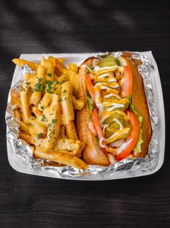 Foil tray with fries and a hot dog topped with ketchup, mustard, onions, and peppers