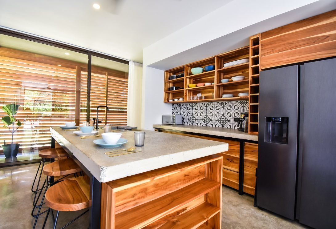 Modern kitchen with a wooden island, open shelving, and a large black refrigerator.