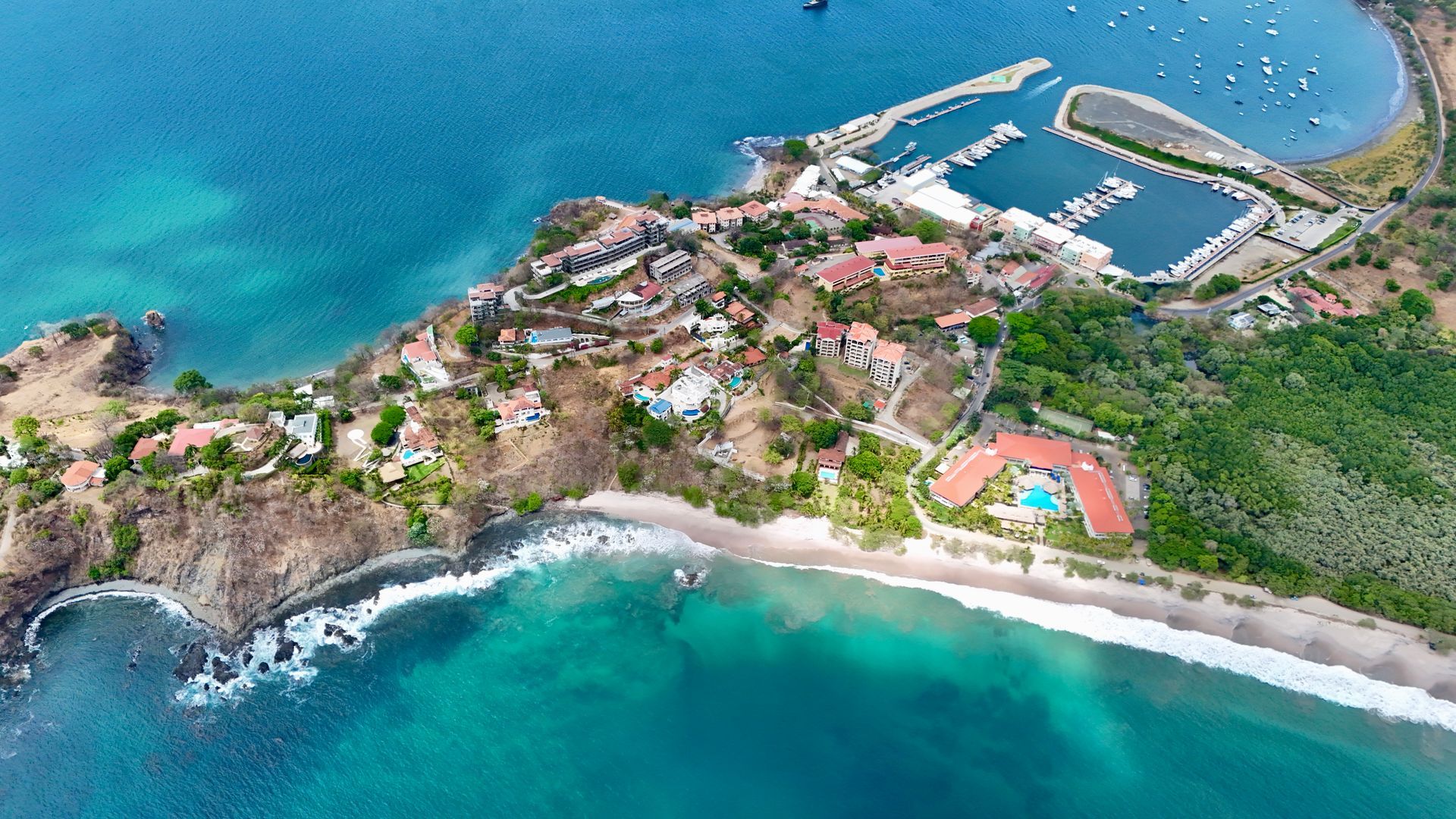 Coastal view with buildings, marina, and beach, surrounded by turquoise water.