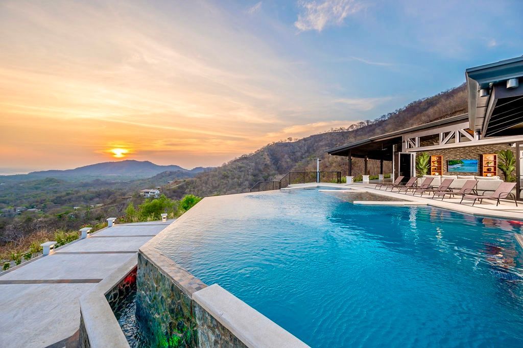 Infinity pool overlooking mountains and ocean at sunset.