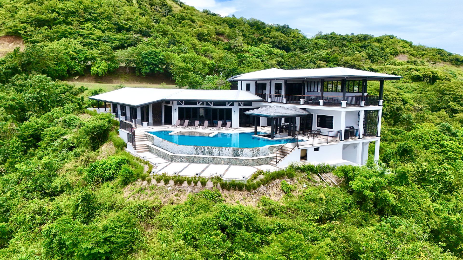 White luxury villa with pool nestled in lush green hillside.