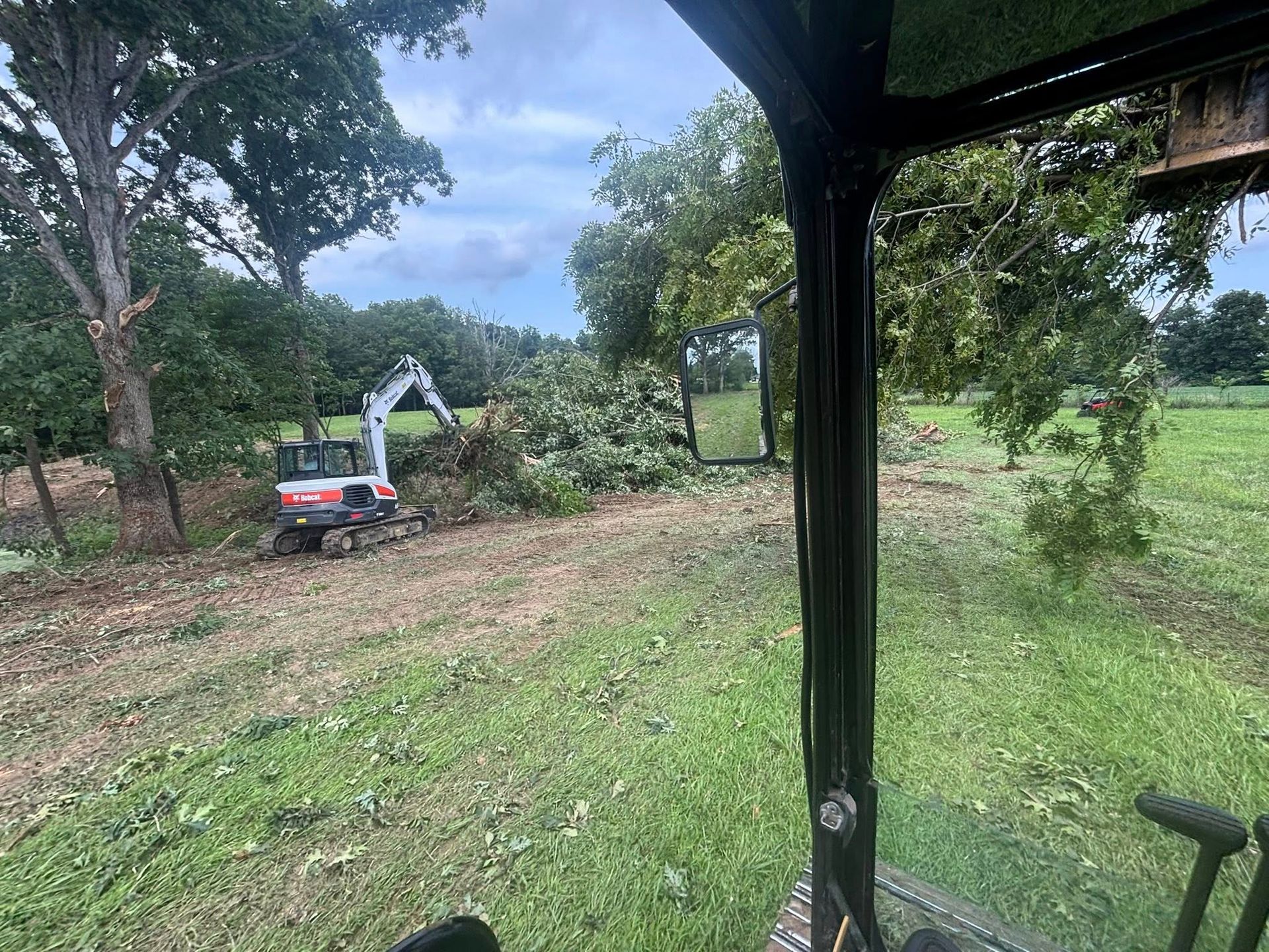 An excavator clears a wooded area; seen from inside another vehicle.