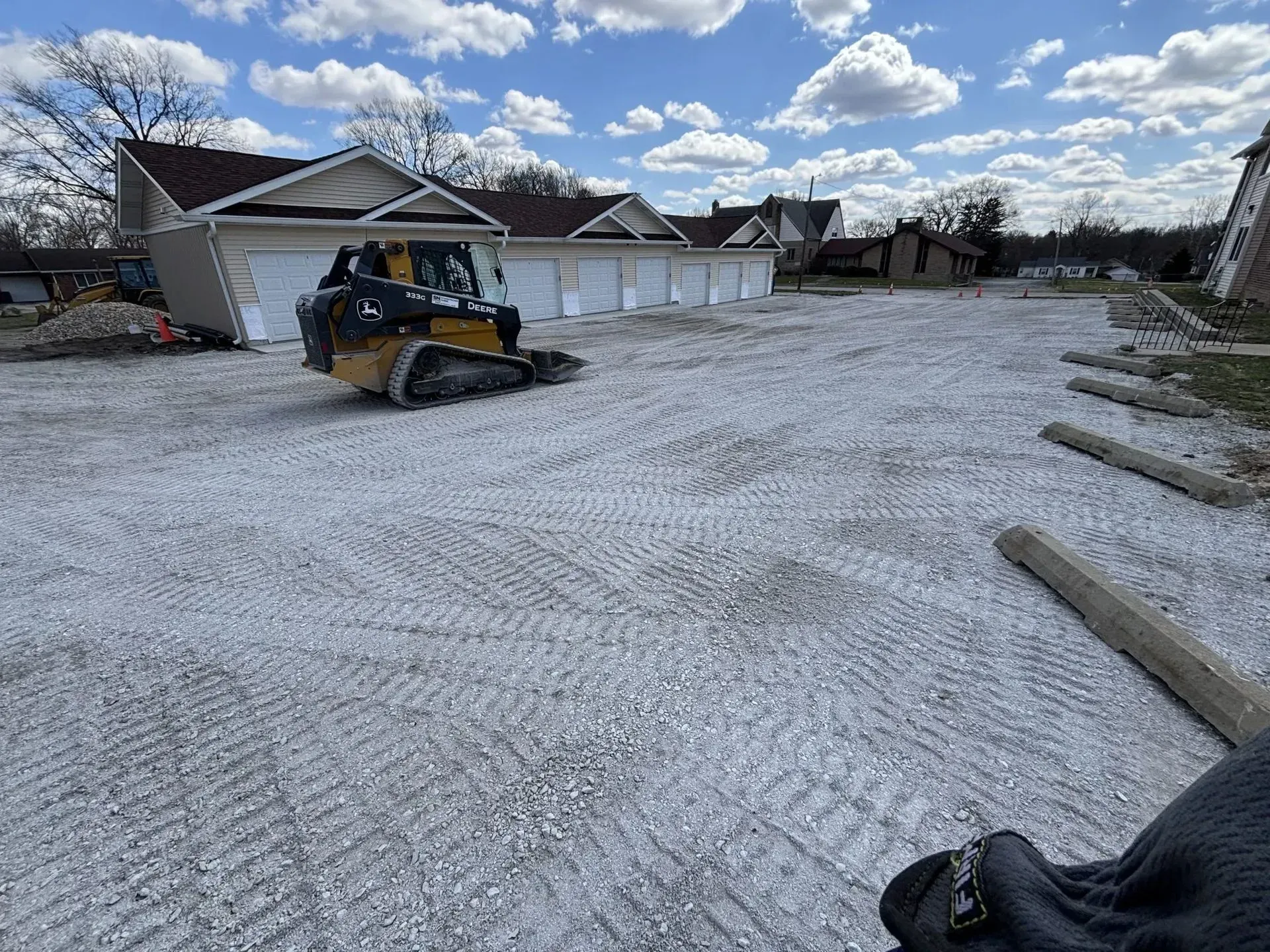 Construction site with a skid steer grading gravel. Garage in background.