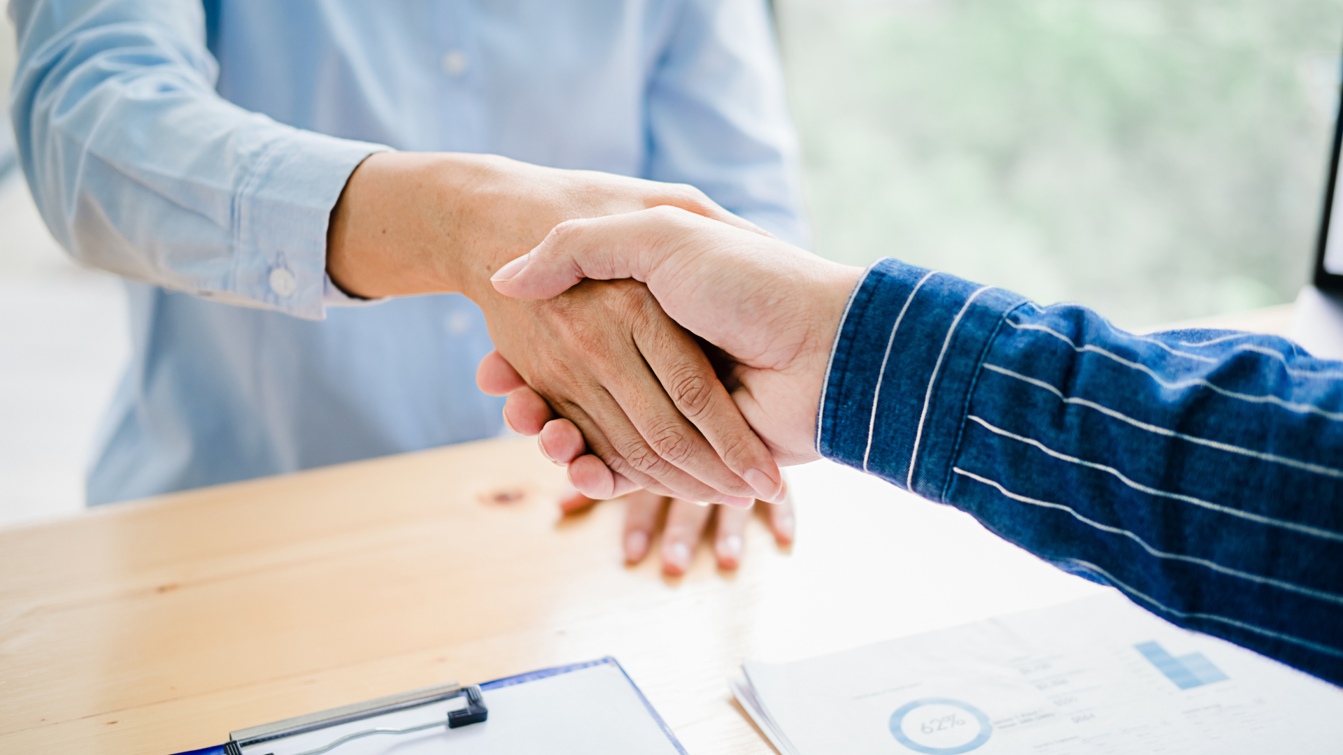 Two men are shaking hands over a wooden table.
