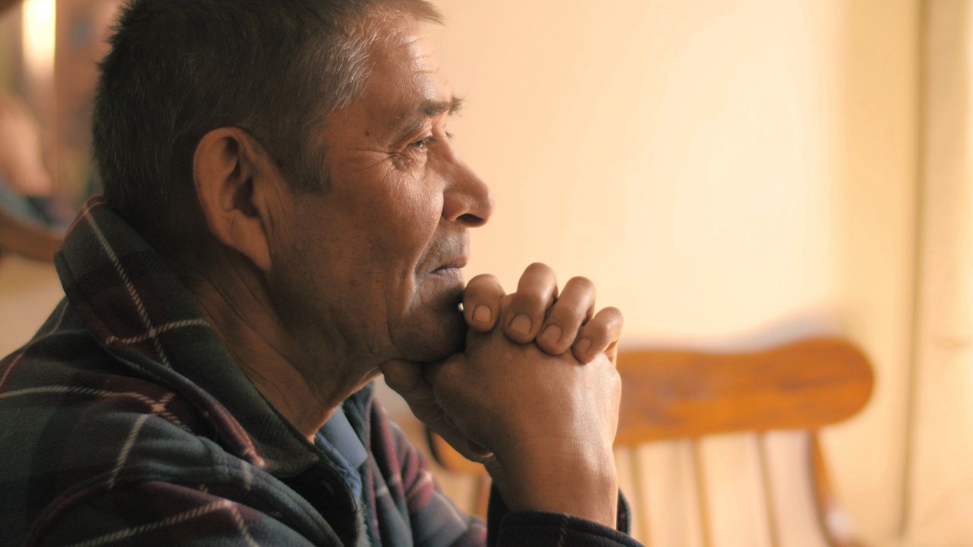 Grieving man in plaid shirt sitting in chair with head resting in his hands.