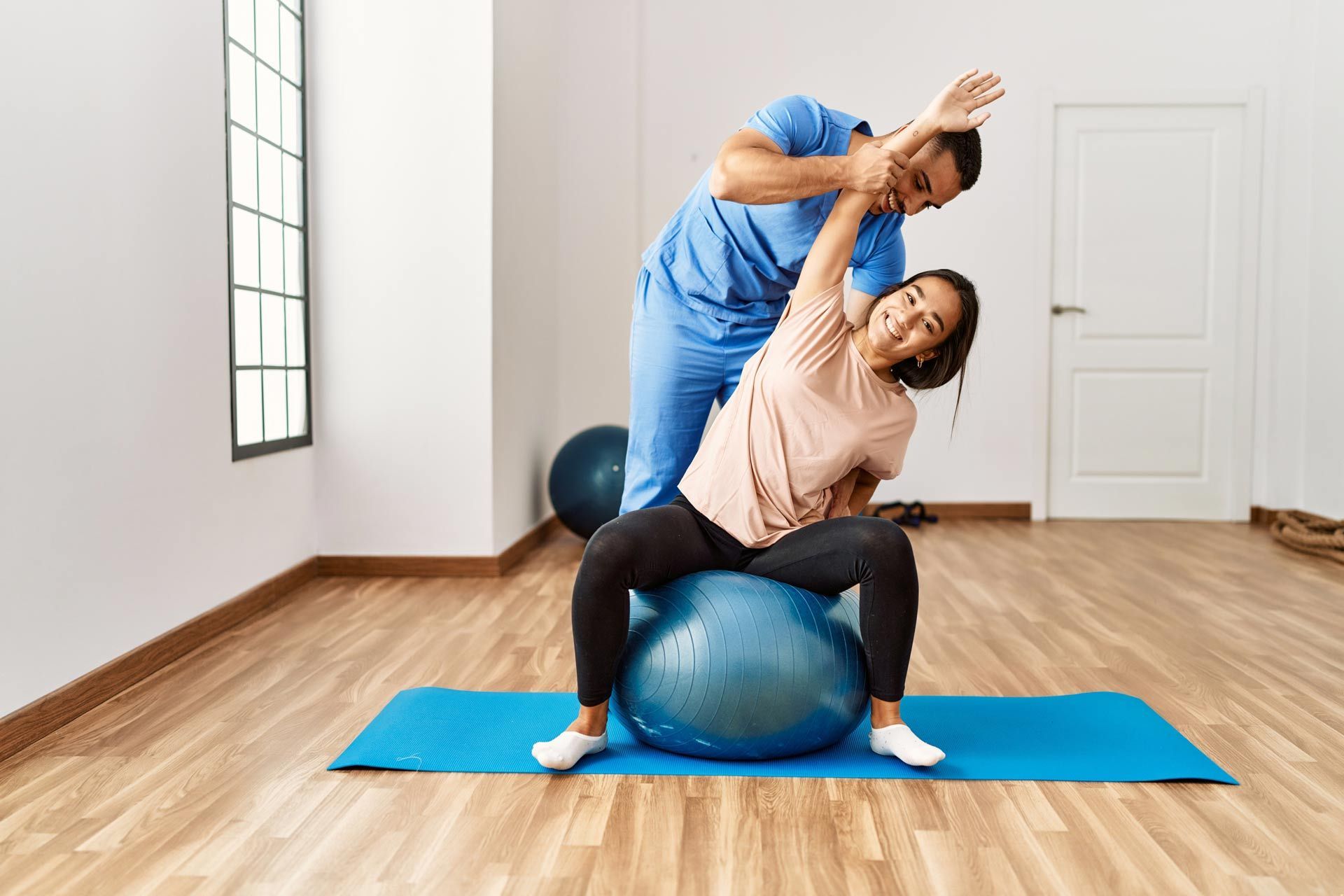 Latin-man-and-woman-wearing-physiotherapist-uniform-having-rehab-session-using-fit-ball-at-rehab-center