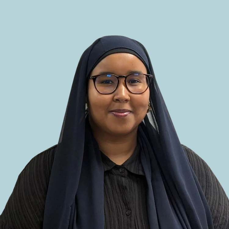 Woman in a dark hijab and glasses, smiling, set against a blue background.