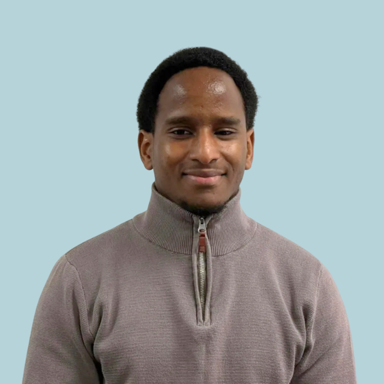 Man in a light gray sweater smiles, against a light blue background.