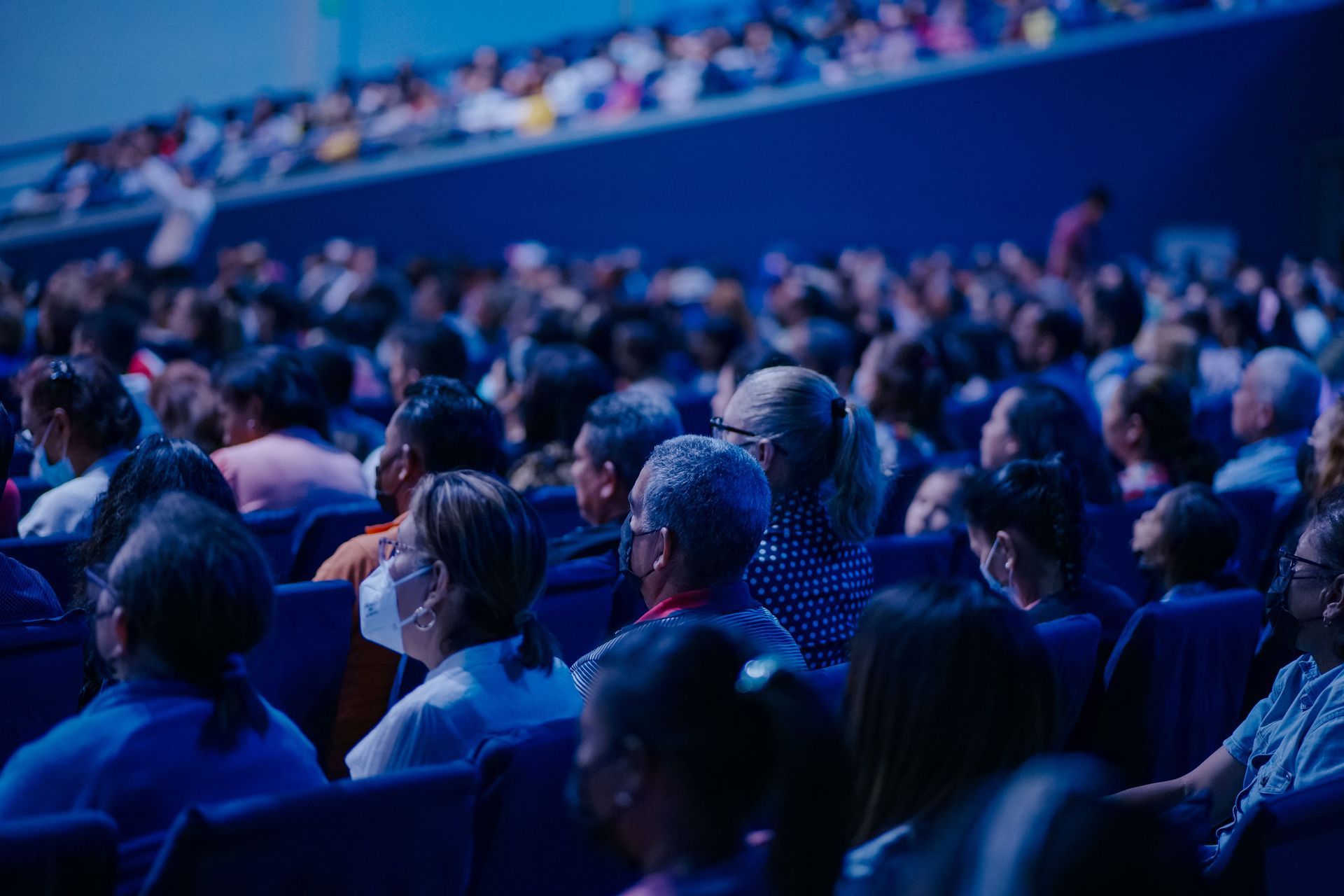 Audience seated in a dim blue-lit auditorium, watching a presentation