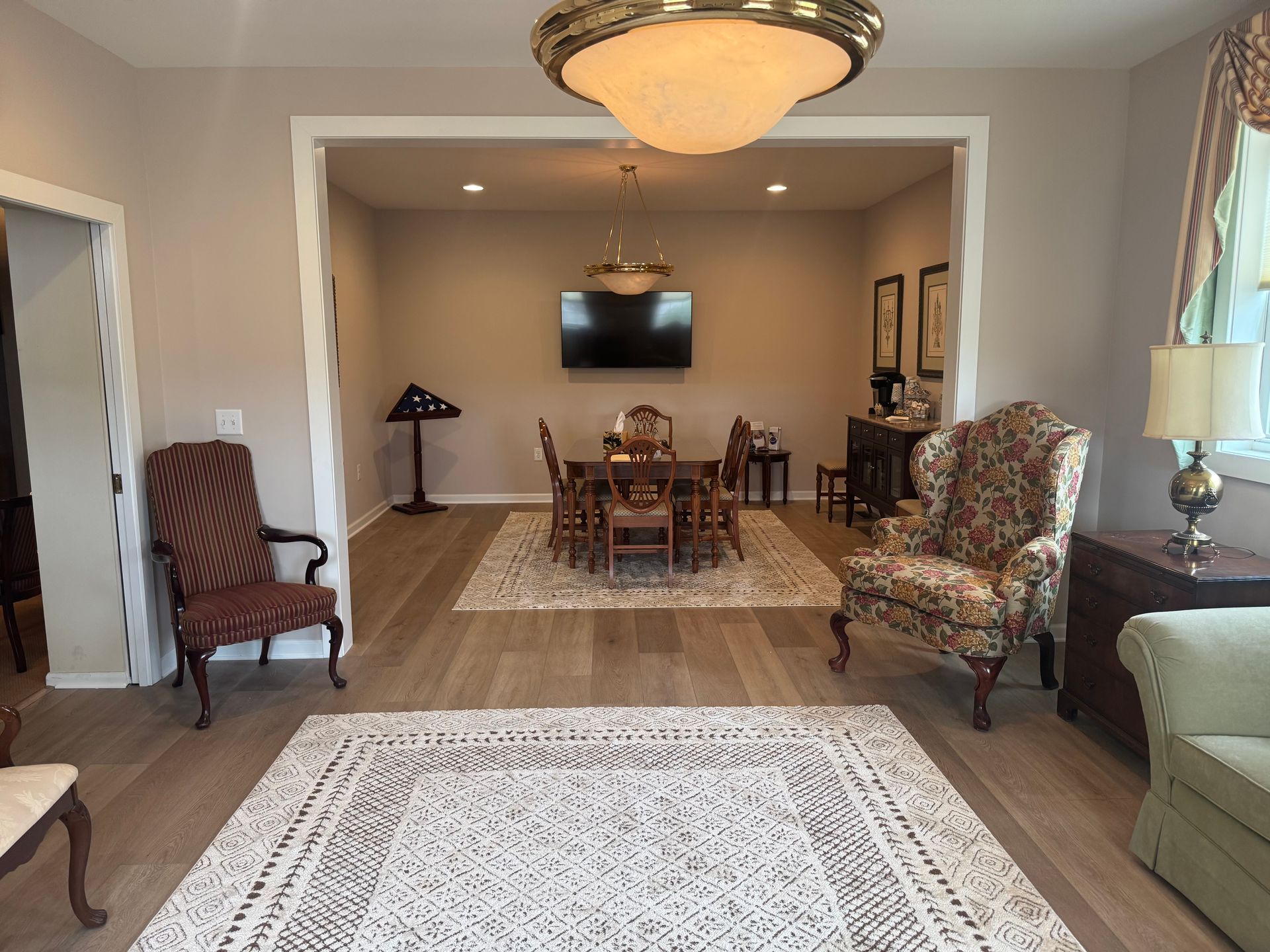 Living room opening to dining area with chairs, rug, lamps, and wall-mounted TV