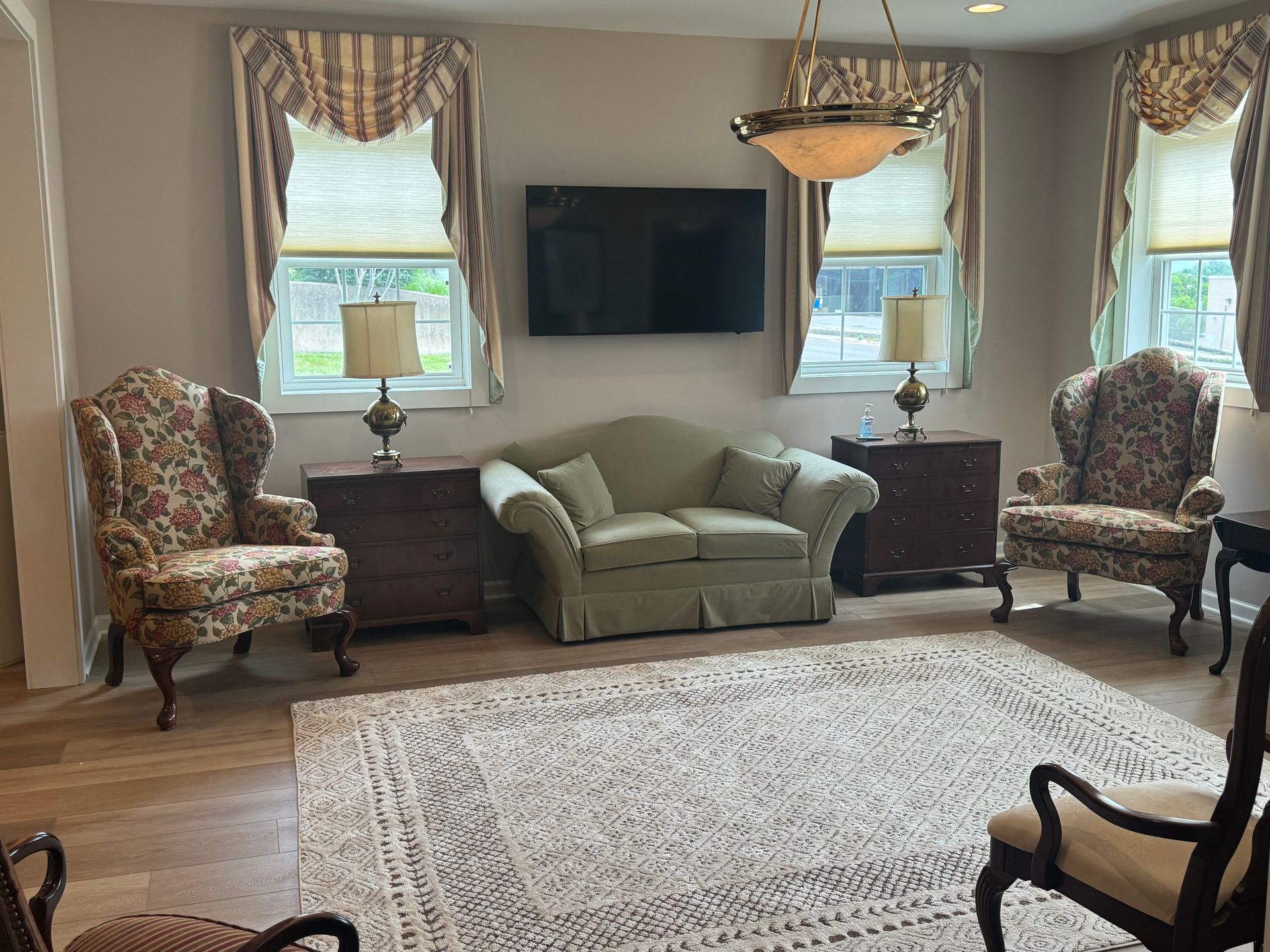 Living room with two patterned armchairs, green loveseat, TV, windows, lamp, and large rug