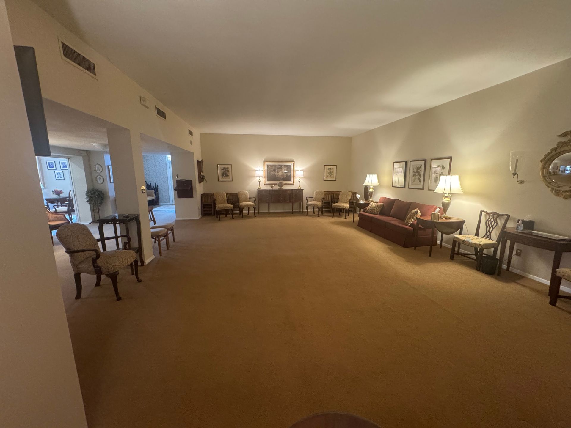 Spacious beige living room with sofas, chairs, lamps, and wall art under soft lighting