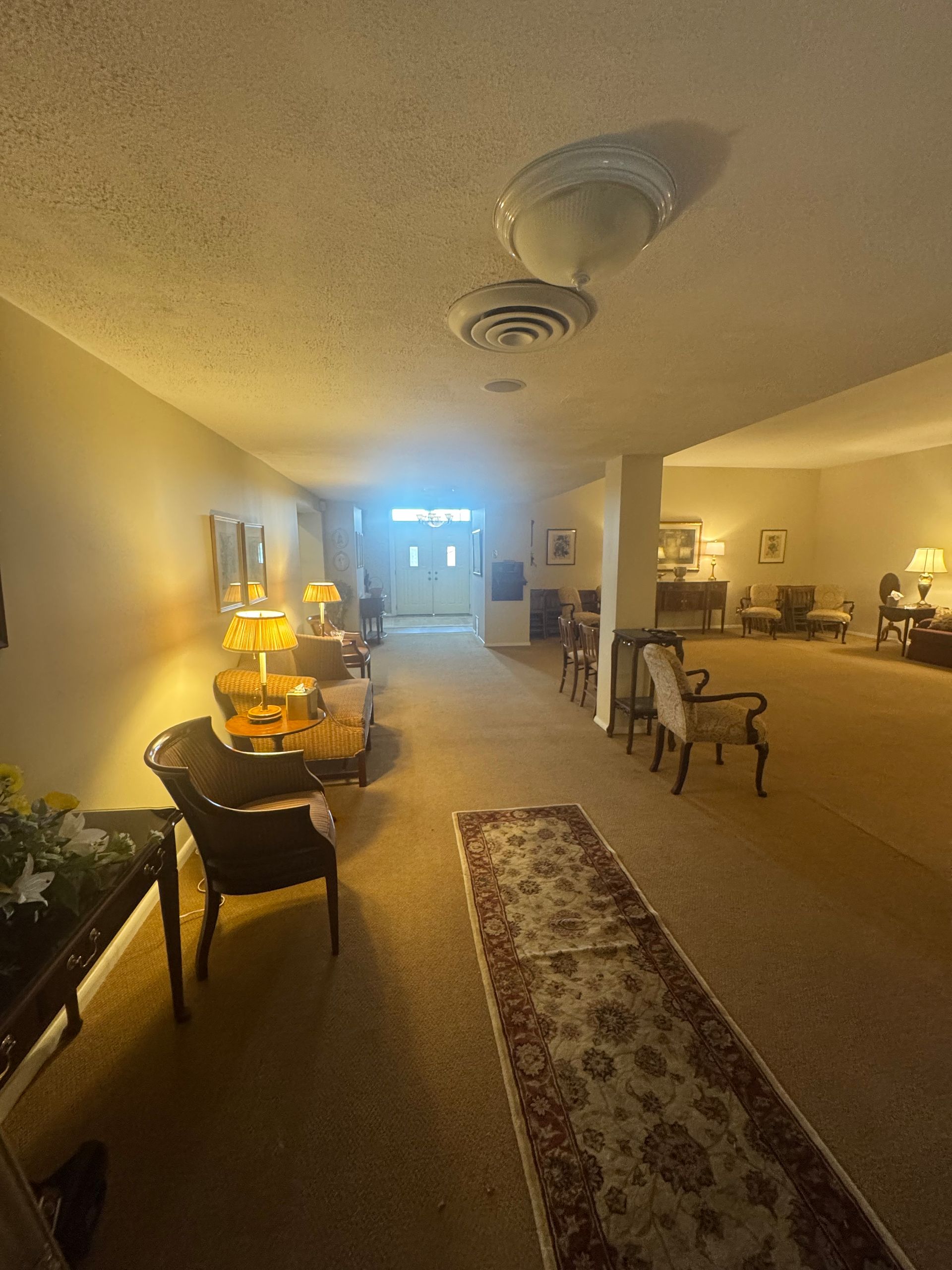 Warmly lit living room with chairs, rugs, and lamps stretching toward a bright doorway