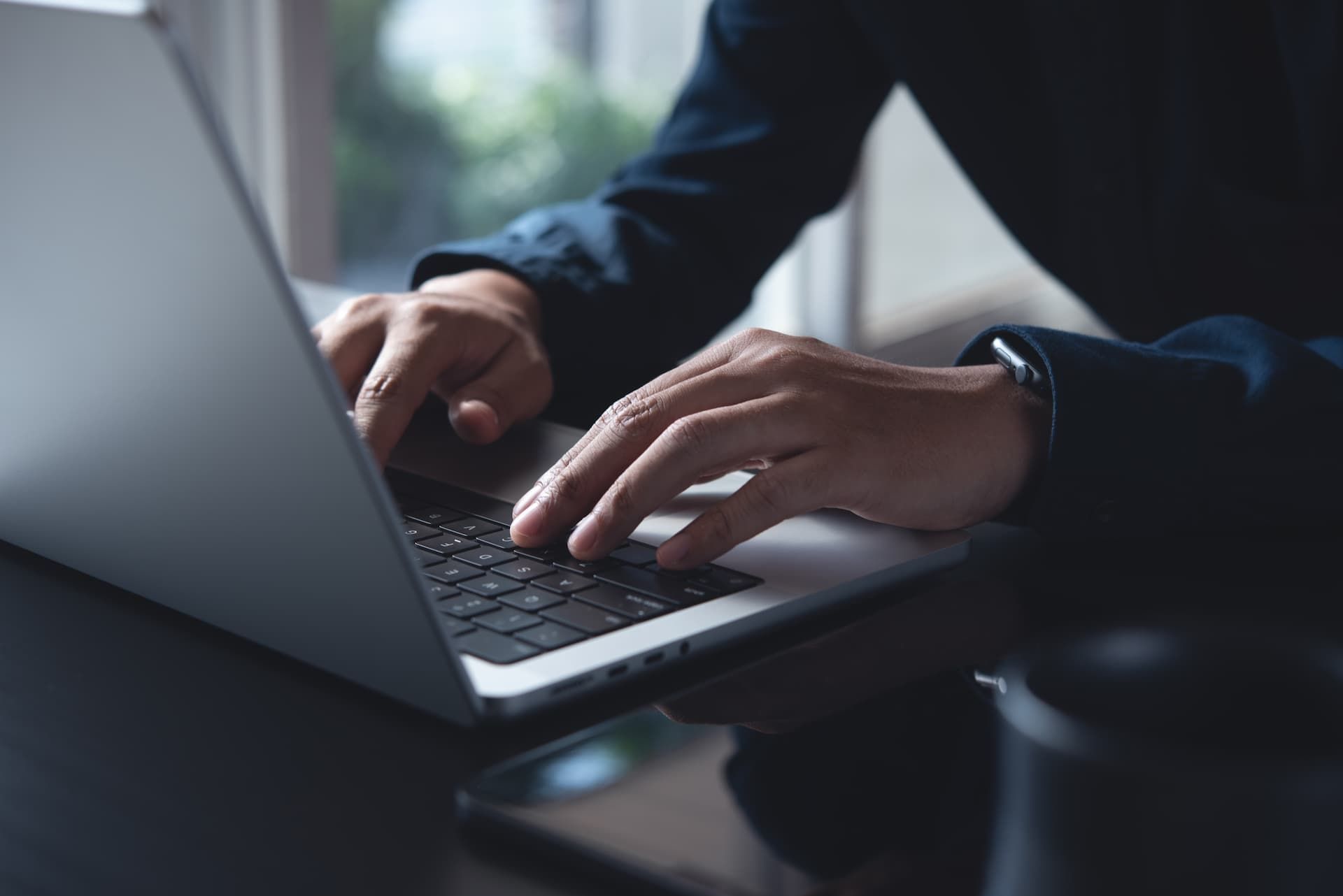 Hands typing on a laptop in a dimly lit workspace