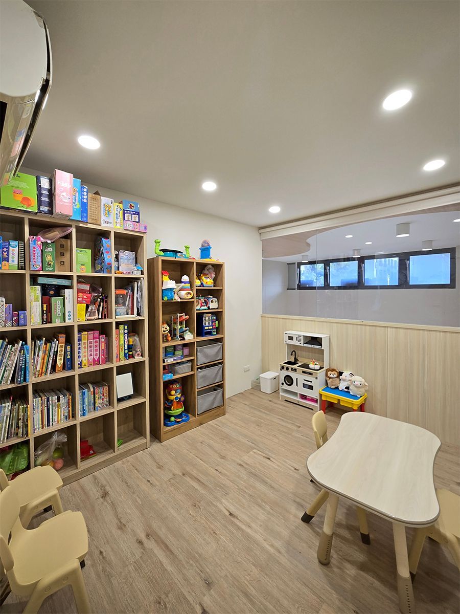 遊戲室有書架、小桌椅和玩具。木地板，白色牆壁。