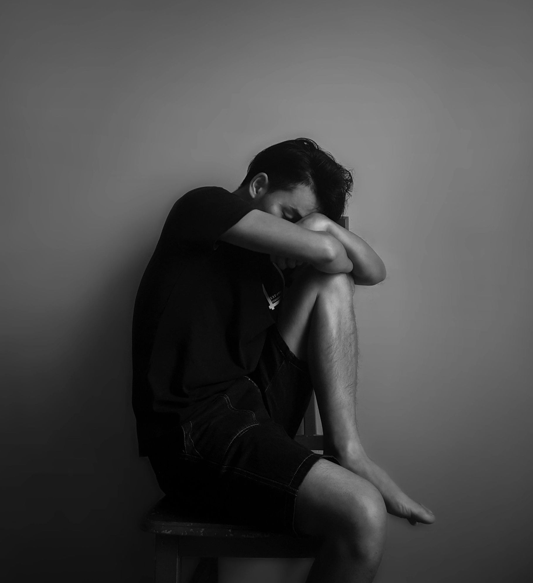 一名身穿短褲的男子坐著,頭靠在膝蓋上,蜷縮在昏暗的房間裡,看起來很痛苦。