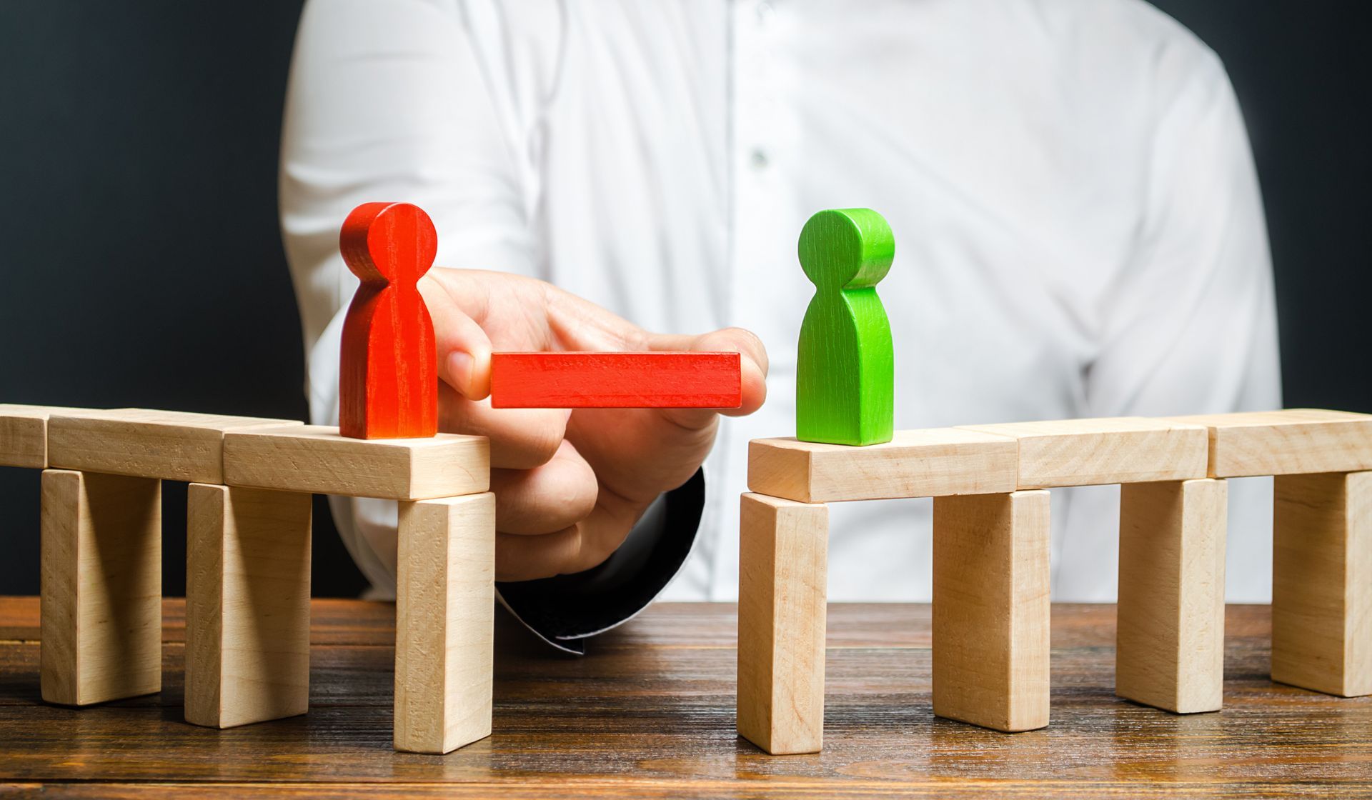 Mediation service concept with a hand placing a connecting block between two wooden figures. Mediation service concept with a hand placing a connecting block between two wooden figures.