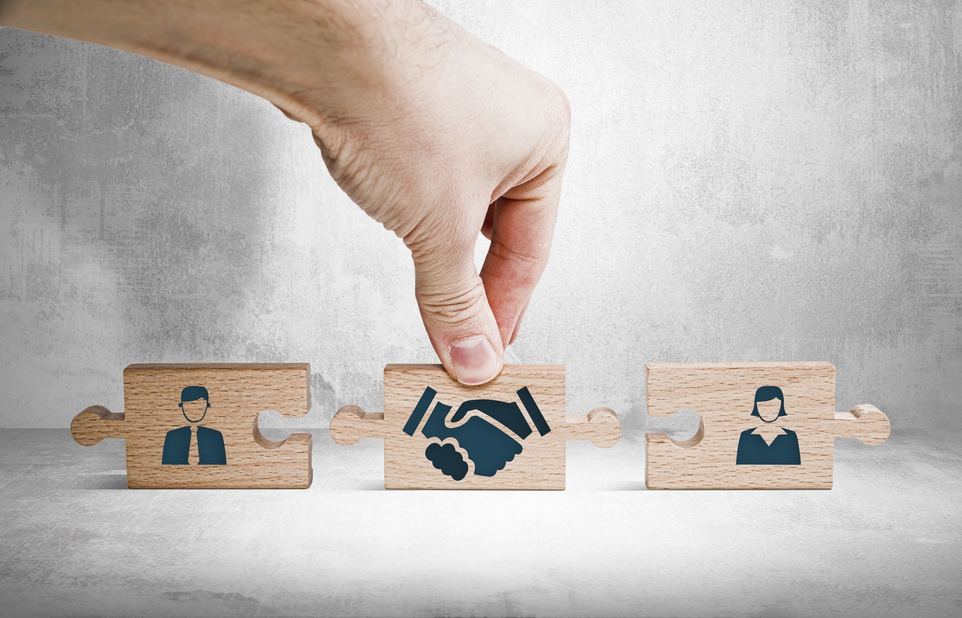 Hand placing puzzle piece with handshake icon between two people icons on blocks.