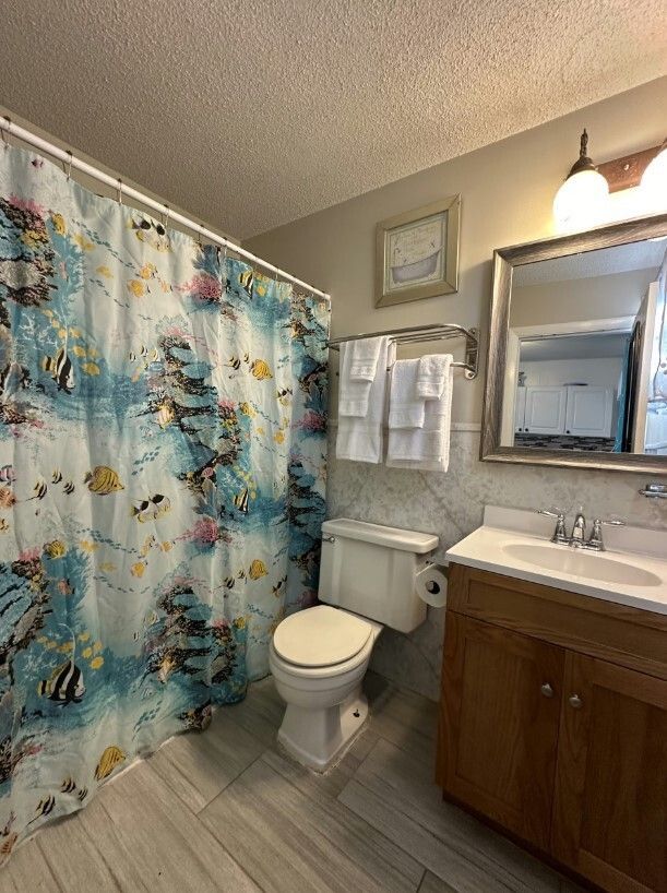A bathroom with light gray wood-look floors, a white toilet, a wooden vanity with a mirror, and a colorful fish-patterned.