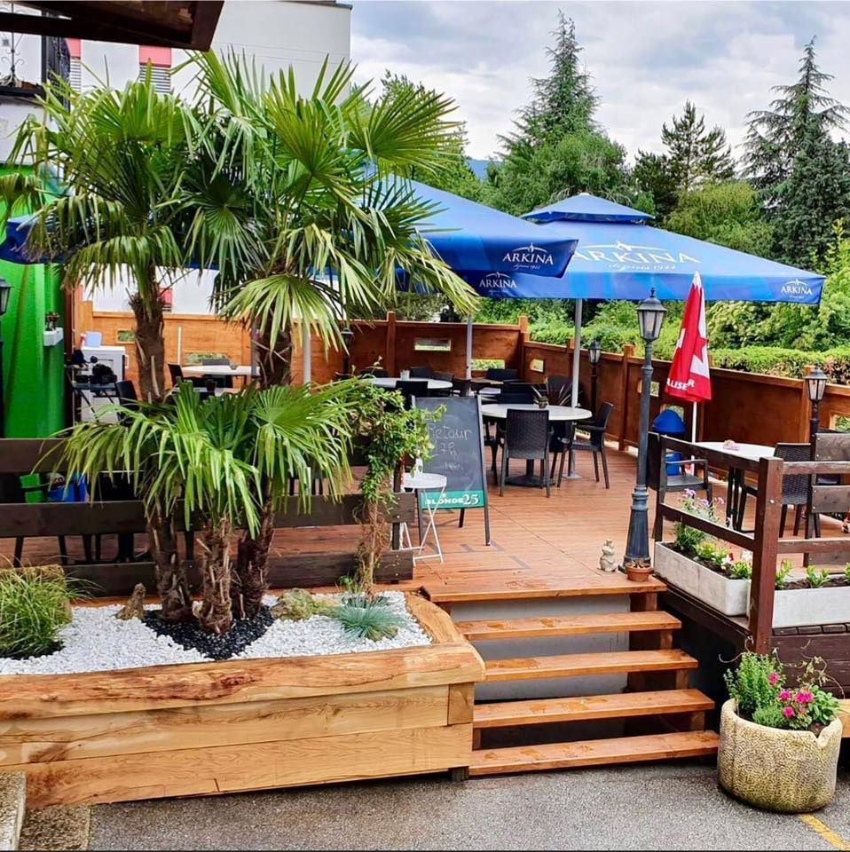 Un patio avec des tables et des chaises et un parasol bleu avec écrit aquafina