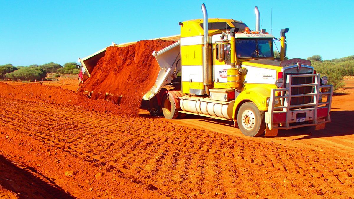 A yellow and white side tipper truck unloading dirt.