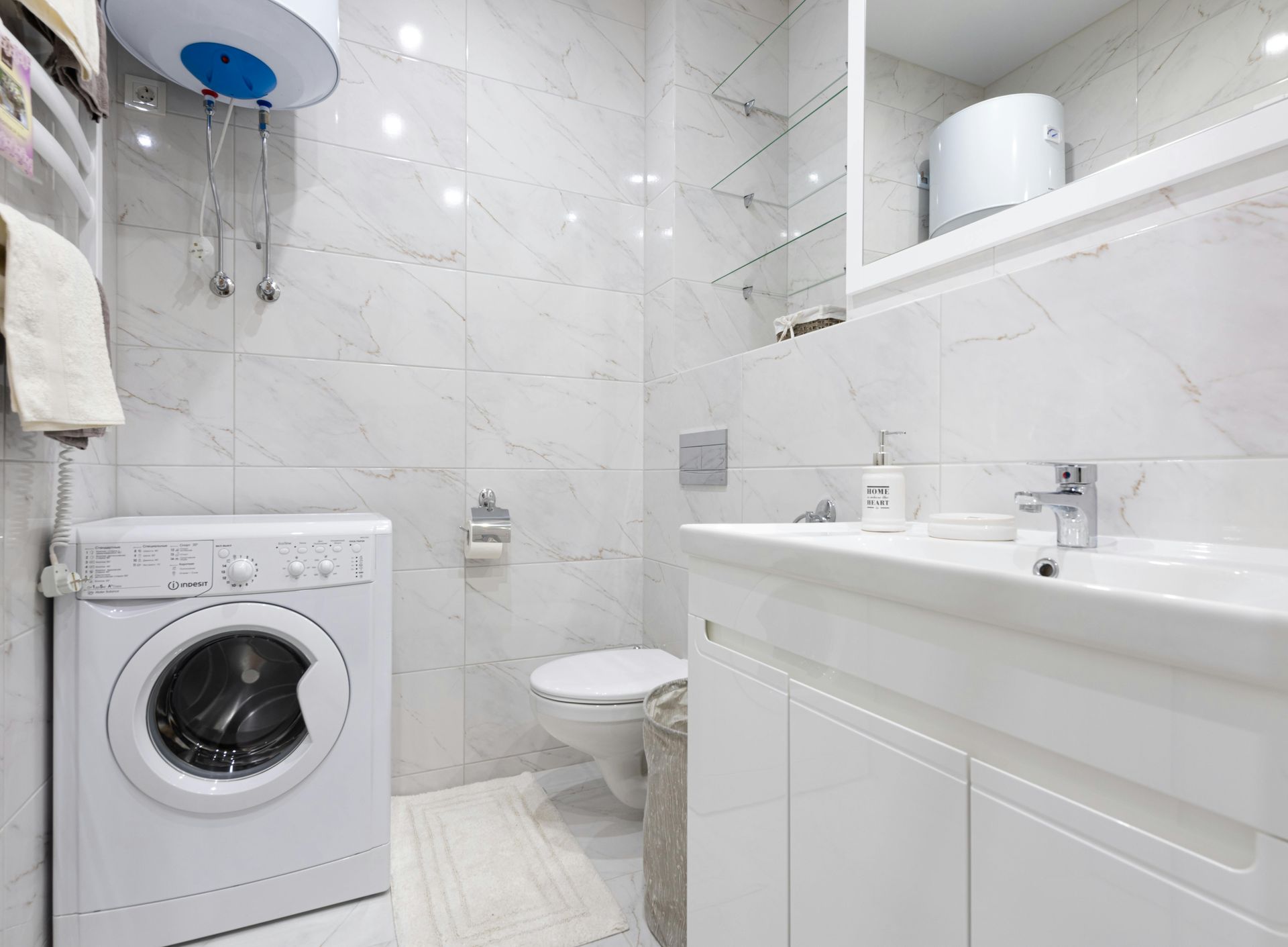 Small white bathroom with a washing machine, toilet, sink, and shower stall.