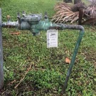 Outdoor water meter with green pipes and a hanging tag in a grassy yard