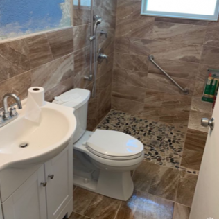 Small bathroom with sink, toilet, and walk-in shower tiled in brown stone and pebble floor