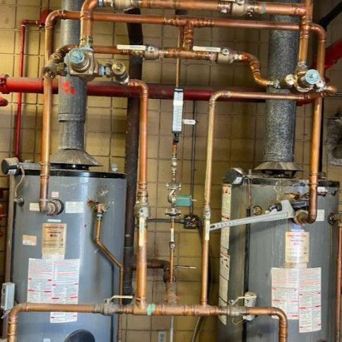 Two tall water heaters with copper pipes and valves in a utility room