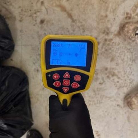 Handheld yellow-and-black thermal camera aimed at a dusty floor by gloved hands