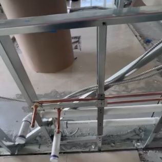 Construction site with exposed pipes, metal framing, and a large duct in a partially built wall