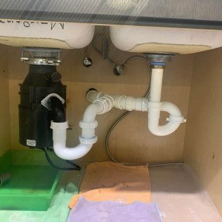 Under-sink plumbing with white drain pipes, a black garbage disposal, and a green tray beneath the sink.