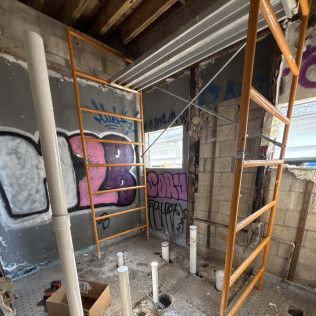 Scaffolded graffiti-covered room with exposed pipes and construction debris on the floor