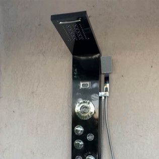 Black shower panel with overhead rainfall head and control knobs against a beige wall