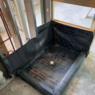 Partially waterproofed shower stall with black membrane lining and a drain in the center