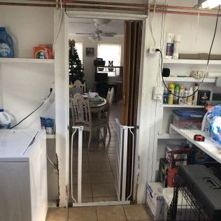 Small kitchen doorway with white shelves, tiled floor, and a Christmas tree visible in the next room.
