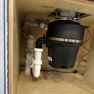 Under-sink plumbing with a black garbage disposal and white PVC drain pipes.