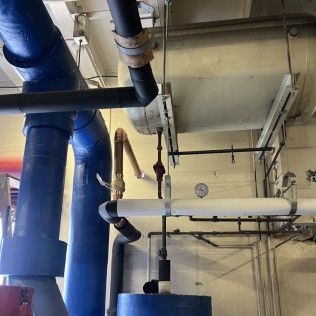 Industrial ceiling with large blue and black pipes and hanging valves in a utility room