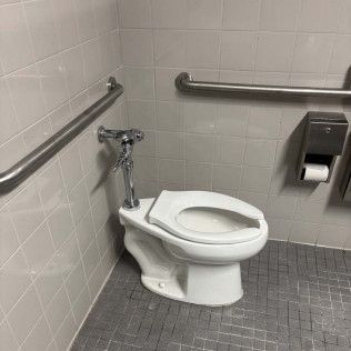 Accessible public restroom with a toilet, grab bars, and tiled walls and floor.