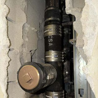 Close-up of plumbing pipes and a valve inside a torn wall opening