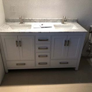 White double-sink bathroom vanity with gray cabinets and a marble countertop against a light wall.