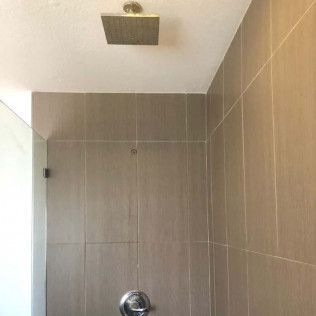 Small tiled shower stall with beige walls and a ceiling-mounted showerhead.