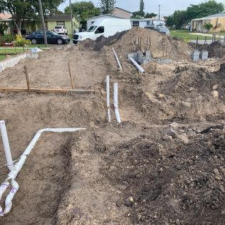 Trenches at a construction site with exposed soil and white PVC pipes running through them.