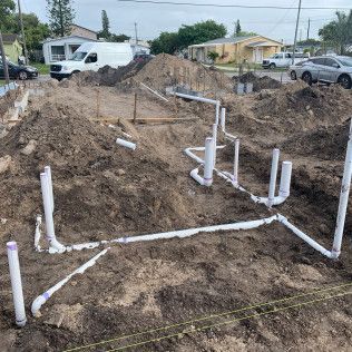 Plumbed foundation trench at a construction site with white PVC pipes in the dirt.