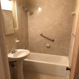 Small beige bathroom with a sink, bathtub, showerhead, and grab bar.
