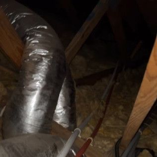 Attic with silver insulated ducting, wooden beams, and a pair of pliers in the foreground