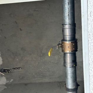 Metal gas pipe with a yellow shutoff valve against a gray wall indoors
