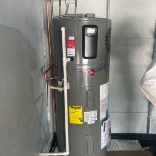 Water heater in a utility closet with copper pipes and a gray wall.