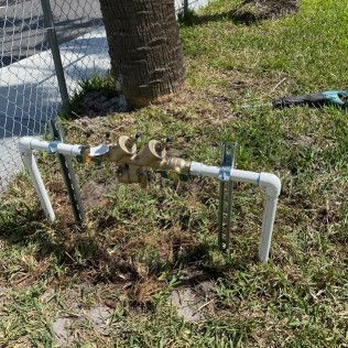 Outdoor PVC pipe assembly with valves and fittings beside a chain-link fence and tree stump in grass