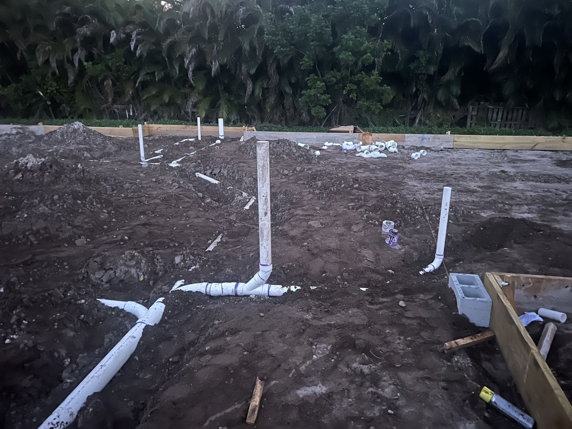 Excavated dirt lot with white PVC pipes and wooden forms laid out for utility or foundation work.
